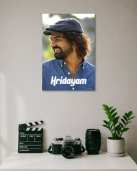 Hridayam Movie Poster Featuring Pranav Mohanlal poster design: Pranav Mohanlal wears a flat cap and blue shirt in this portrait inspired by Hridayam. White lettering across the lower section displays the film title, giving the design a clean, understated look for Malayalam cinema fans.